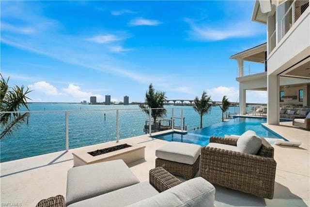280 Estrellita Dr, Fort Myers Beach, FL 33931 View of swimming pool with a water view, an outdoor living space with a fire pit, an infinity pool, and patio surround - Virtually Edited Image