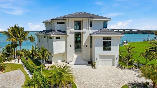 280 Estrellita Dr, Fort Myers Beach, FL 33931 View of front facade featuring a water view, a tile roof, a garage, and decorative driveway - Virtually Edited Image