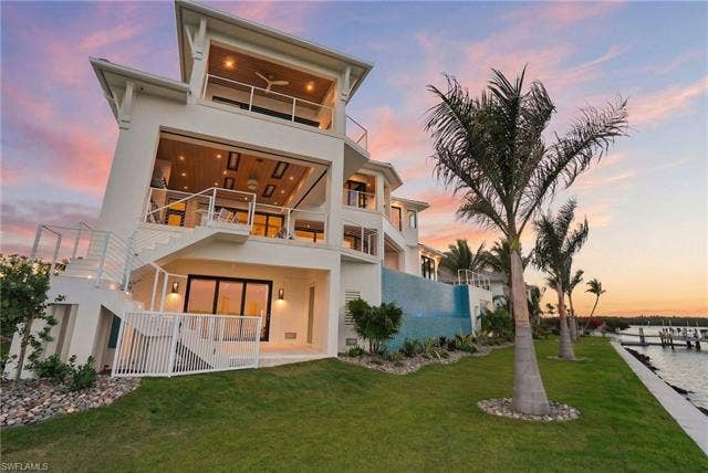 280 Estrellita Dr, Fort Myers Beach, FL 33931 Back of house at dusk featuring a balcony, a patio, stucco siding, and a yard - Virtually Edited Image