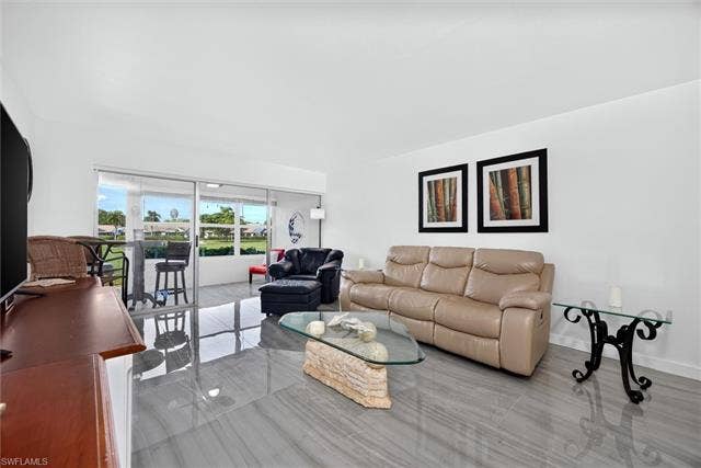 6220 Augusta Dr, #117, Fort Myers, FL 33907 Spacious living area featuring large format tile flooring, white walls, and sliding glass doors opening to an enclosed patio
