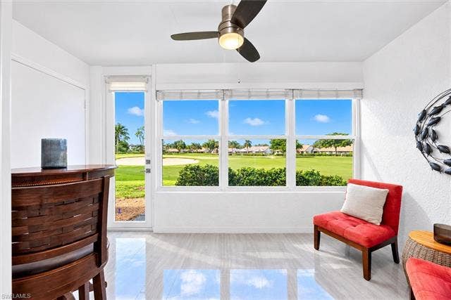 6220 Augusta Dr, #117, Fort Myers, FL 33907 Expansive window wall with golf course scenery, sliding glass door access, light-toned tile flooring, and a ceiling fan