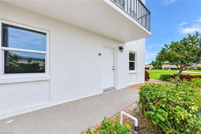 6220 Augusta Dr, #117, Fort Myers, FL 33907 White exterior with textured stucco finish, featuring a contemporary light fixture, a concrete walkway, and landscaped shrubbery