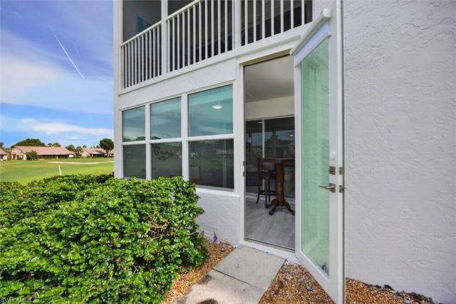 6220 Augusta Dr, #117, Fort Myers, FL 33907 Ground-level entry with an open glass door, a wall of windows, and an upper-level balcony featuring white railings