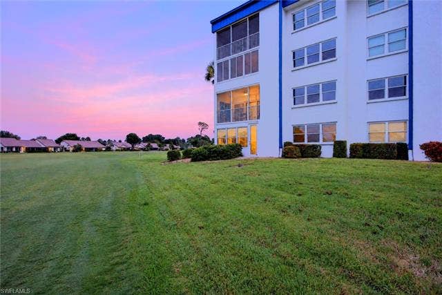 6220 Augusta Dr, #117, Fort Myers, FL 33907 Multi-story building with white exterior and blue trim, featuring screened-in balconies and multiple windows, alongside a manicured green lawn
