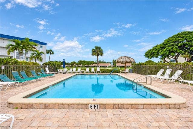 6220 Augusta Dr, #117, Fort Myers, FL 33907 Rectangular swimming pool surrounded by paver decking, equipped with handrails and a thatched-roof cabana