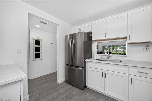 6220 Augusta Dr, #117, Fort Myers, FL 33907 Contemporary kitchen featuring white cabinetry, light-toned countertops, a stainless steel refrigerator, and a stainless steel sink with a high-arc faucet