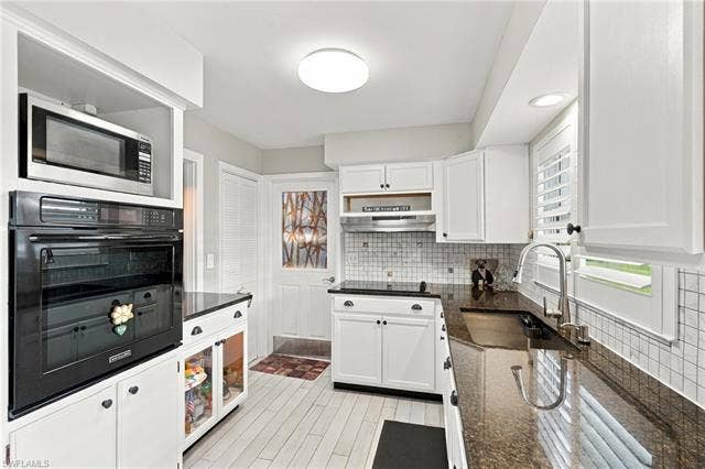 2816 18th Ave, Cape Coral, FL 33904 White cabinetry with black hardware, built-in oven and microwave, dark stone countertops, tile backsplash, and wood-finish flooring
