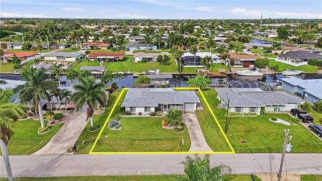 2816 18th Ave, Cape Coral, FL 33904 Waterfront property with a private dock, mature palm trees, a spacious green lawn, and an attached garage