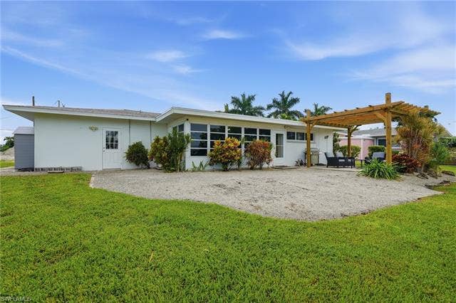 2816 18th Ave, Cape Coral, FL 33904 Expansive gravel patio with a built-in wooden pergola, complemented by a manicured lawn and mature landscaping