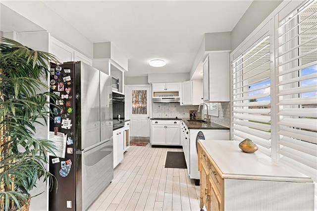 2816 18th Ave, Cape Coral, FL 33904 White cabinetry with dark countertops, white wood-finish flooring, plantation shutters, and a mosaic tile backsplash