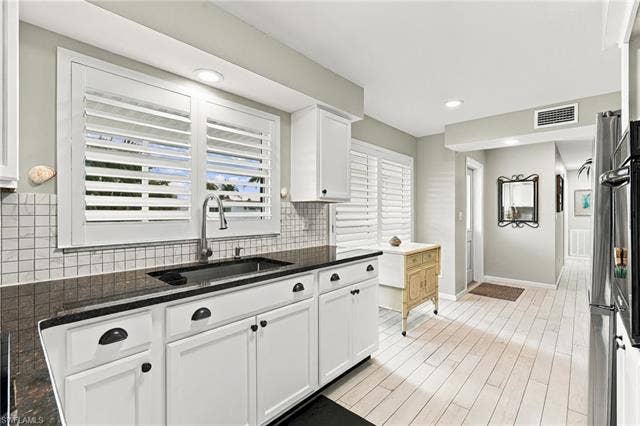 2816 18th Ave, Cape Coral, FL 33904 White cabinetry with black hardware, dark countertops, a tiled backsplash, plantation shutters, and light wood-finish flooring