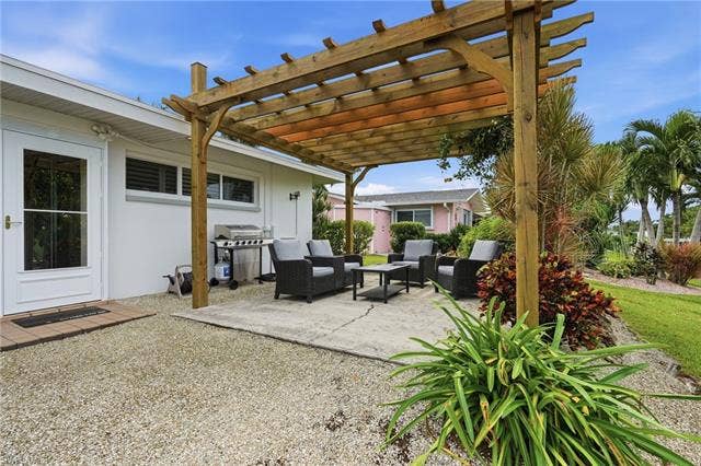 2816 18th Ave, Cape Coral, FL 33904 Wood pergola covering a concrete patio, bordered by gravel landscaping and green foliage