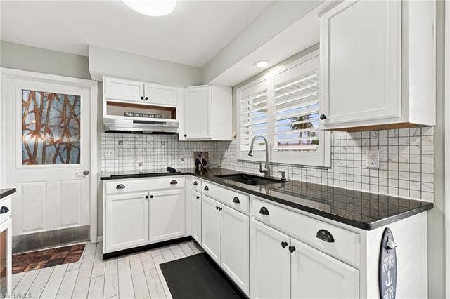 2816 18th Ave, Cape Coral, FL 33904 White cabinetry with black hardware, dark countertops, a tile backsplash, and wood-finish flooring