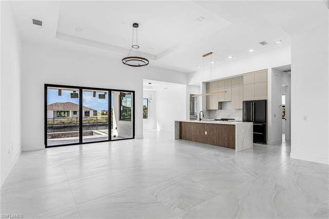 4116 36th Ln, Cape Coral, FL 33993 Expansive white tile flooring, contemporary kitchen island with wood-finish cabinetry and stone waterfall countertop, modern pendant lighting, and large sliding glass doors