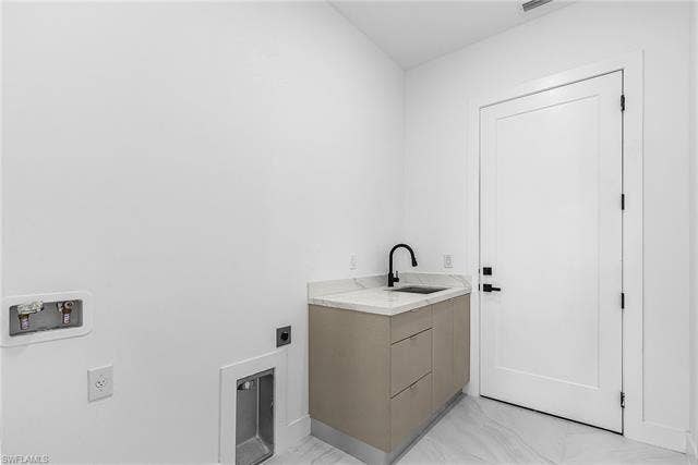 4116 36th Ln, Cape Coral, FL 33993 Laundry area featuring a vanity with a white countertop and integrated sink, matte black faucet, and light-toned cabinetry
