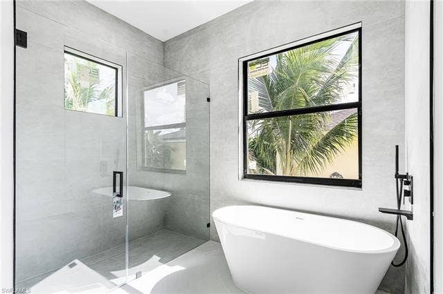 4116 36th Ln, Cape Coral, FL 33993 Freestanding soaking tub with wall-mounted matte black faucet, glass-enclosed shower, large format wall and floor tiling, and black-framed windows