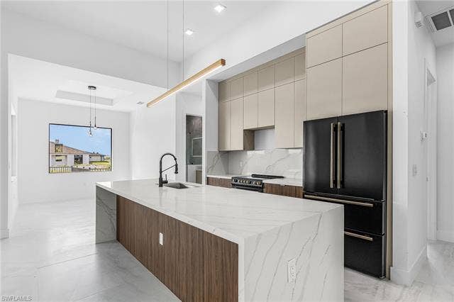 4116 36th Ln, Cape Coral, FL 33993 Kitchen featuring an expansive island with a waterfall countertop, integrated sink, and modern pendant lighting