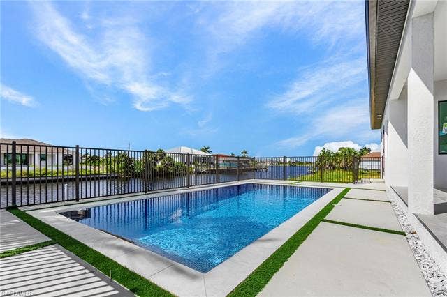 4116 36th Ln, Cape Coral, FL 33993 Rectangular swimming pool with a black metal fence, concrete patio, and a waterfront setting