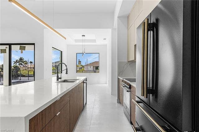 4116 36th Ln, Cape Coral, FL 33993 Kitchen featuring a large island with a white countertop and integrated sink, wood-finish cabinetry, black and gold-tone appliances, and recessed lighting