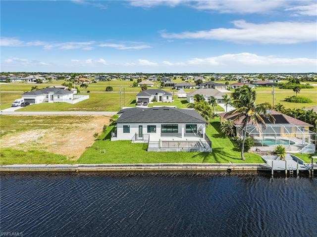 4116 36th Ln, Cape Coral, FL 33993 Modern home with an expansive backyard featuring a waterfront concrete seawall, a raised deck, and a private dock with boat lift