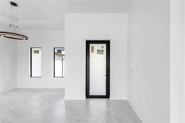 4116 36th Ln, Cape Coral, FL 33993 Tray ceiling with a contemporary chandelier, two vertical windows, and a frosted glass entry door