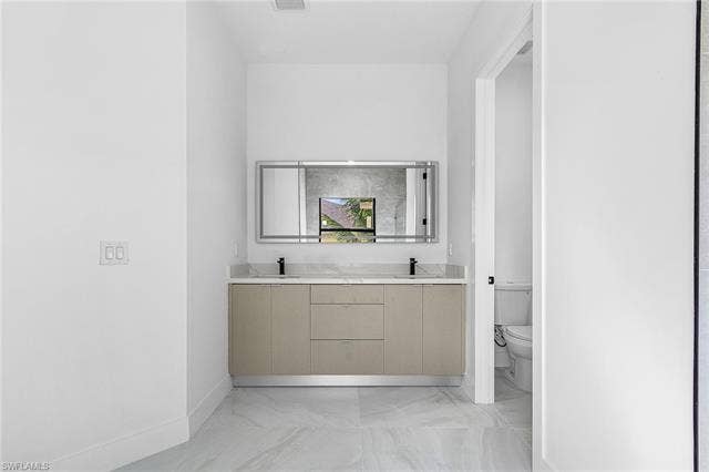 4116 36th Ln, Cape Coral, FL 33993 Dual vanity with stone countertop, integrated sinks, matte black fixtures, and a mirrored medicine cabinet