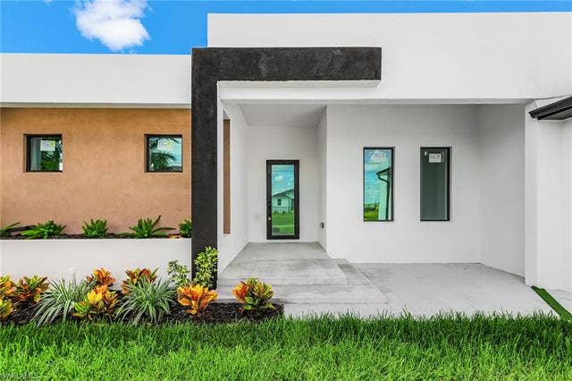 4116 36th Ln, Cape Coral, FL 33993 Modern facade with a flat roofline, contrasting dark and light stucco finishes, black-framed windows, and an entrance with a substantial overhang