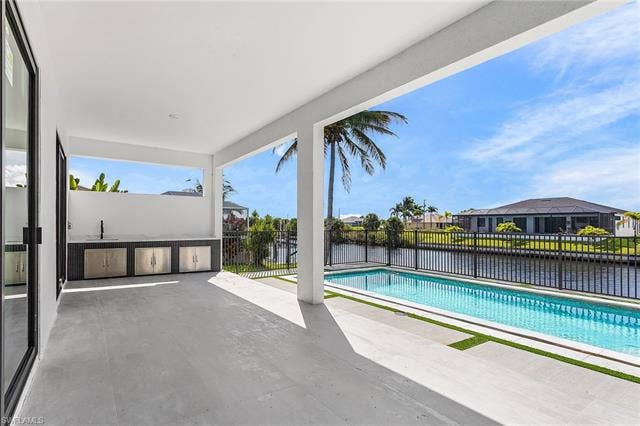 4116 36th Ln, Cape Coral, FL 33993 Covered patio with integrated outdoor kitchen, contemporary swimming pool, water frontage, and black metal fencing