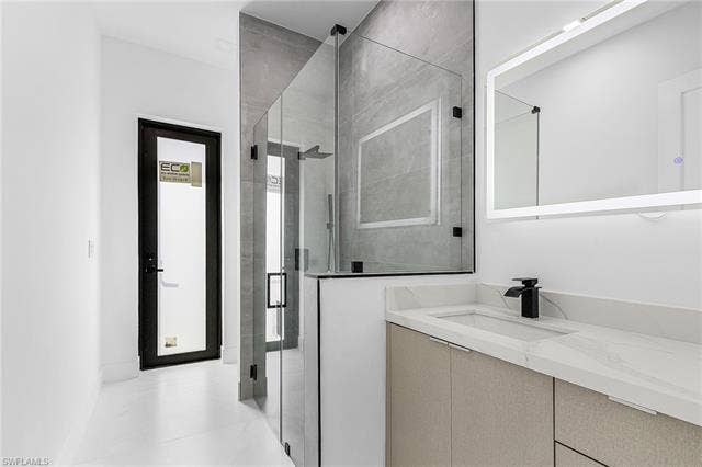 4116 36th Ln, Cape Coral, FL 33993 Modern bathroom featuring a single vanity with a white countertop and undermount sink, matte black faucet, and an illuminated rectangular mirror