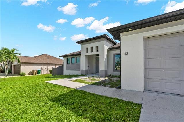 113 38 Pl, Cape Coral, FL 33993 Contemporary exterior with a white and gray facade, a gray paneled garage door, and a manicured lawn