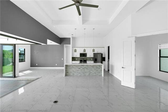 113 38 Pl, Cape Coral, FL 33993 Open-concept living space with large format tile flooring, vaulted ceilings, and a contemporary kitchen featuring an island with a stone veneer facade and pendant lighting
