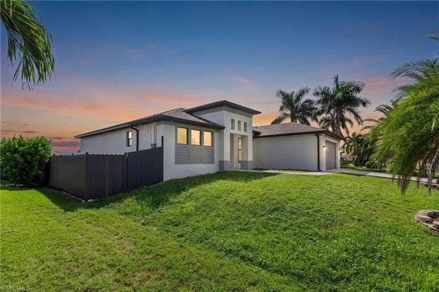 113 38 Pl, Cape Coral, FL 33993 Contemporary architecture featuring a stucco exterior, attached garage, and a lush green lawn