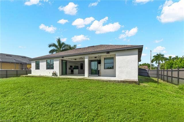 113 38 Pl, Cape Coral, FL 33993 Expansive green lawn with a concrete patio, covered outdoor living space, and a flat-panel fence