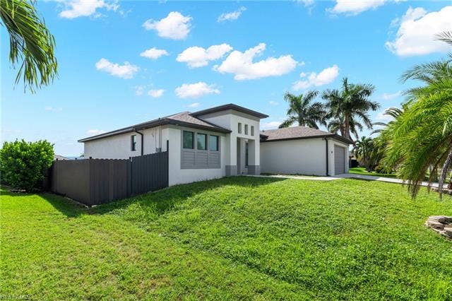113 38 Pl, Cape Coral, FL 33993 Modern stucco exterior with a gray and white color palette, a two-car garage, and established palm trees