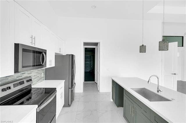 113 38 Pl, Cape Coral, FL 33993 Contemporary kitchen featuring white cabinetry, stainless steel appliances, a tile backsplash, and an island with a built-in sink and pendant lighting