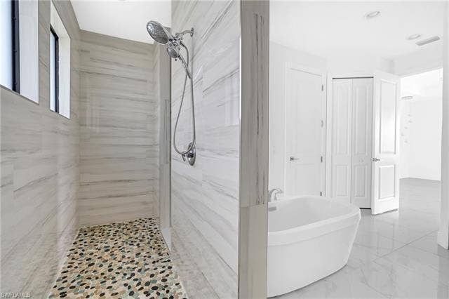 113 38 Pl, Cape Coral, FL 33993 Walk-in shower with natural stone tile walls and pebble flooring, freestanding soaking tub, and contemporary chrome shower fixtures