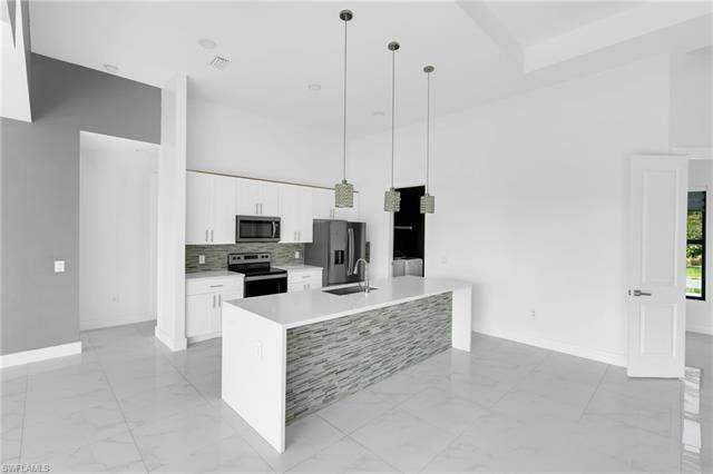 113 38 Pl, Cape Coral, FL 33993 Kitchen featuring white cabinetry, stainless steel appliances, a tile backsplash, and a large island with a waterfall countertop