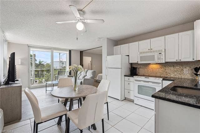 5500 Bonita Beach Rd, #308, Bonita Springs, FL 34134 White cabinetry, dark granite countertops, tile flooring, and a stone-tiled backsplash define the kitchen space