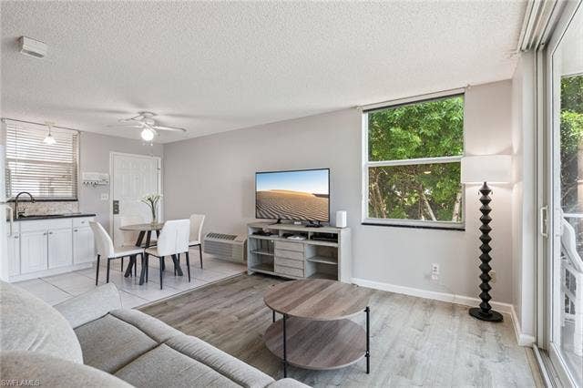 5500 Bonita Beach Rd, #308, Bonita Springs, FL 34134 Open-concept living space featuring wood-finish flooring, a wall-mounted air conditioning unit, and a sliding glass door leading to an outdoor area
