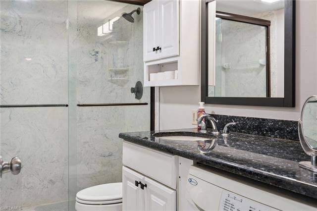 5500 Bonita Beach Rd, #308, Bonita Springs, FL 34134 Glass-enclosed shower with tiled walls and matte black fixtures, vanity with a dark polished countertop and undermount sink, white cabinetry with dark hardware, and a framed mirror