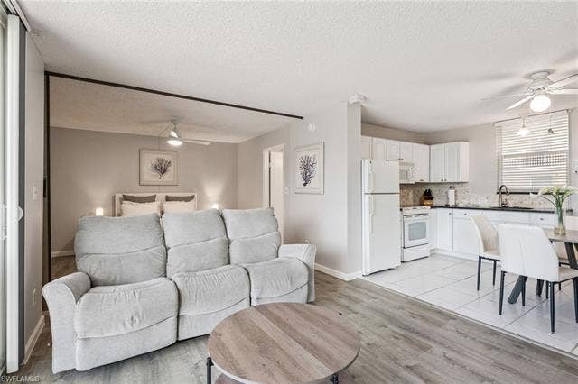 5500 Bonita Beach Rd, #308, Bonita Springs, FL 34134 Open-concept living space with wood-finish flooring, a kitchen featuring white cabinetry and appliances, and a tiled dining area