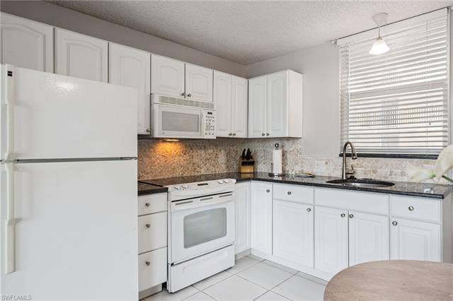 5500 Bonita Beach Rd, #308, Bonita Springs, FL 34134 White cabinetry, dark granite countertops, a mosaic tile backsplash, and a window with blinds