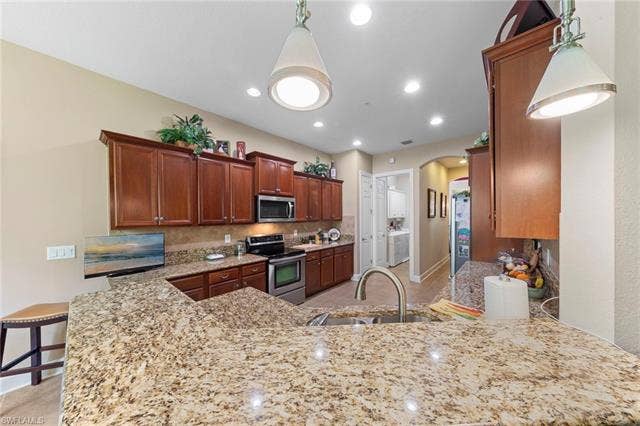 26485 Lucky Stone Rd, #202, Bonita Springs, FL 34135 Kitchen featuring granite countertops, wood-finish cabinetry, stainless steel appliances, recessed lighting, and pendant fixtures