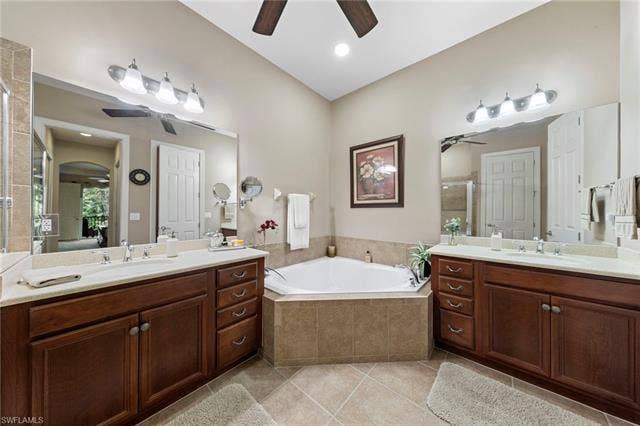26485 Lucky Stone Rd, #202, Bonita Springs, FL 34135 Dual wood-finish vanities with undermount sinks, a corner built-in bathtub with tile surround, and a ceiling fan