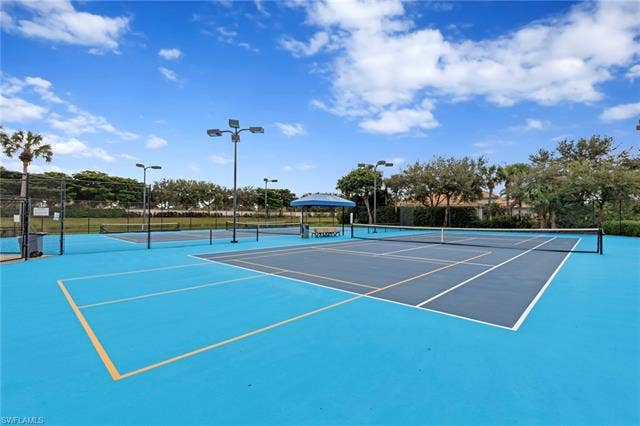 26485 Lucky Stone Rd, #202, Bonita Springs, FL 34135 Multiple tennis courts with blue and gray playing surfaces, perimeter fencing, and overhead lighting fixtures