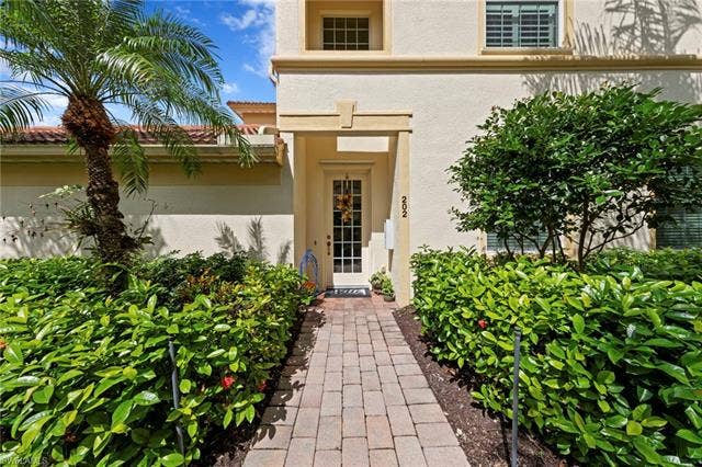 26485 Lucky Stone Rd, #202, Bonita Springs, FL 34135 Paver walkway framed by mature landscaping, leading to a front entry with a glass-paneled door