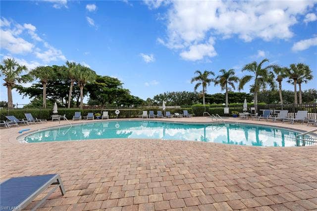 26485 Lucky Stone Rd, #202, Bonita Springs, FL 34135 Resort-style pool area featuring a large curvilinear pool, extensive paver decking, and surrounding mature palm trees