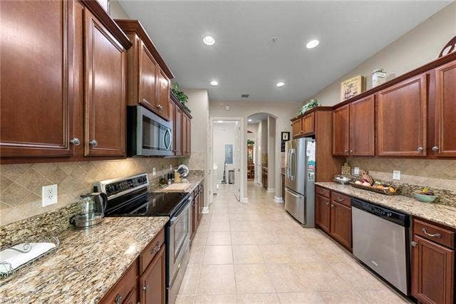 26485 Lucky Stone Rd, #202, Bonita Springs, FL 34135 Galley kitchen featuring wood cabinetry, granite countertops, stainless steel appliances, tile flooring, and a tiled backsplash
