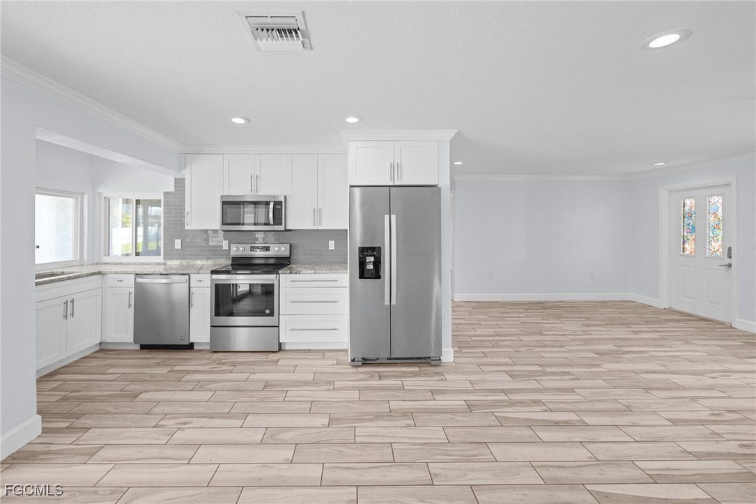 2514 SE 26th Avenue, Cape Coral, FL 33904 Kitchen featuring crown molding, appliances with stainless steel finishes, white cabinets, decorative backsplash, and wood finish floors