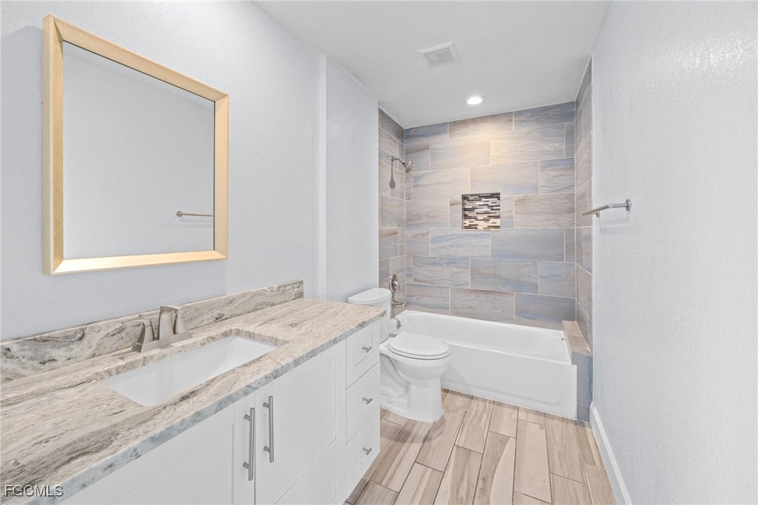 2514 SE 26th Avenue, Cape Coral, FL 33904 Bathroom featuring vanity, washtub / shower combination, wood finish floors, a textured wall, and recessed lighting